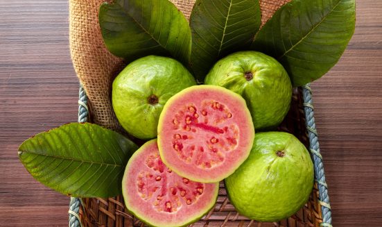 Closeup on red guava sliced with green leaf on rustic wooden background.