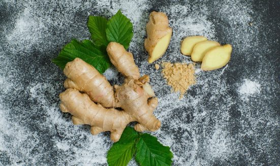 Top view ginger with slices and leaves on gray textured background. horizontal