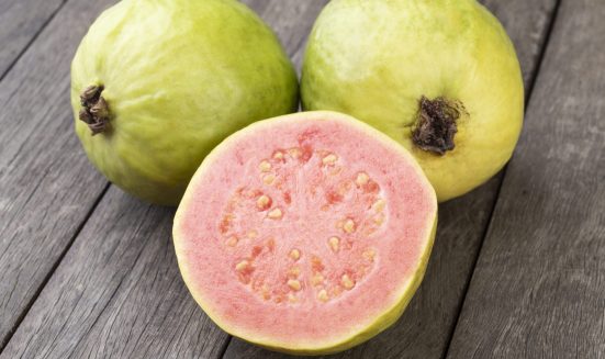 Two guavas with sliced fruit over wooden table.